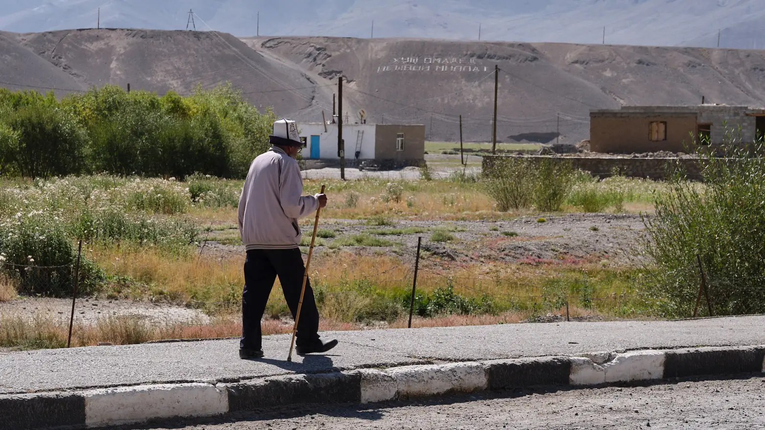 chlapík s holí a kyrgyzskou čepičkou jdoucí po chodníku
