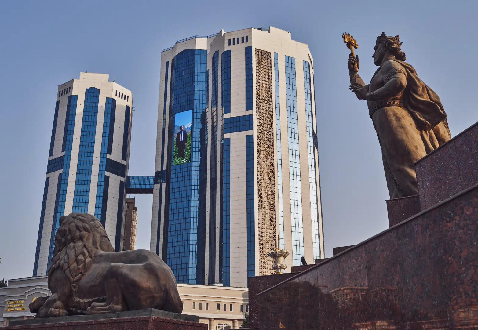 výšková budova s portrétem a sochou v popředí