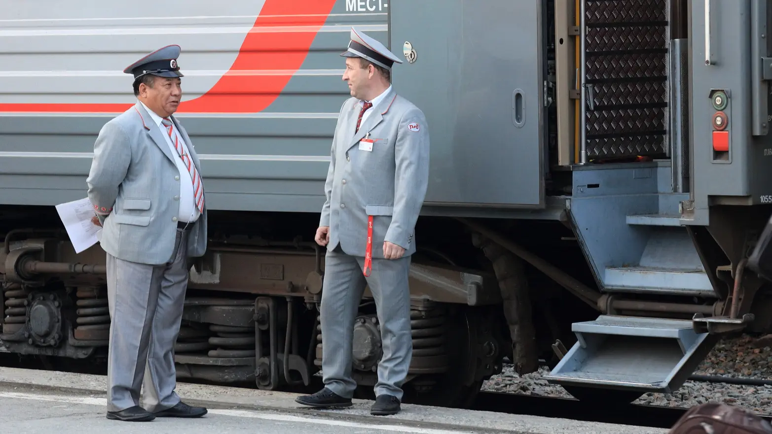 dva železničáři v úhledných uniformách postávají před otevřenými dveřmi vagonu